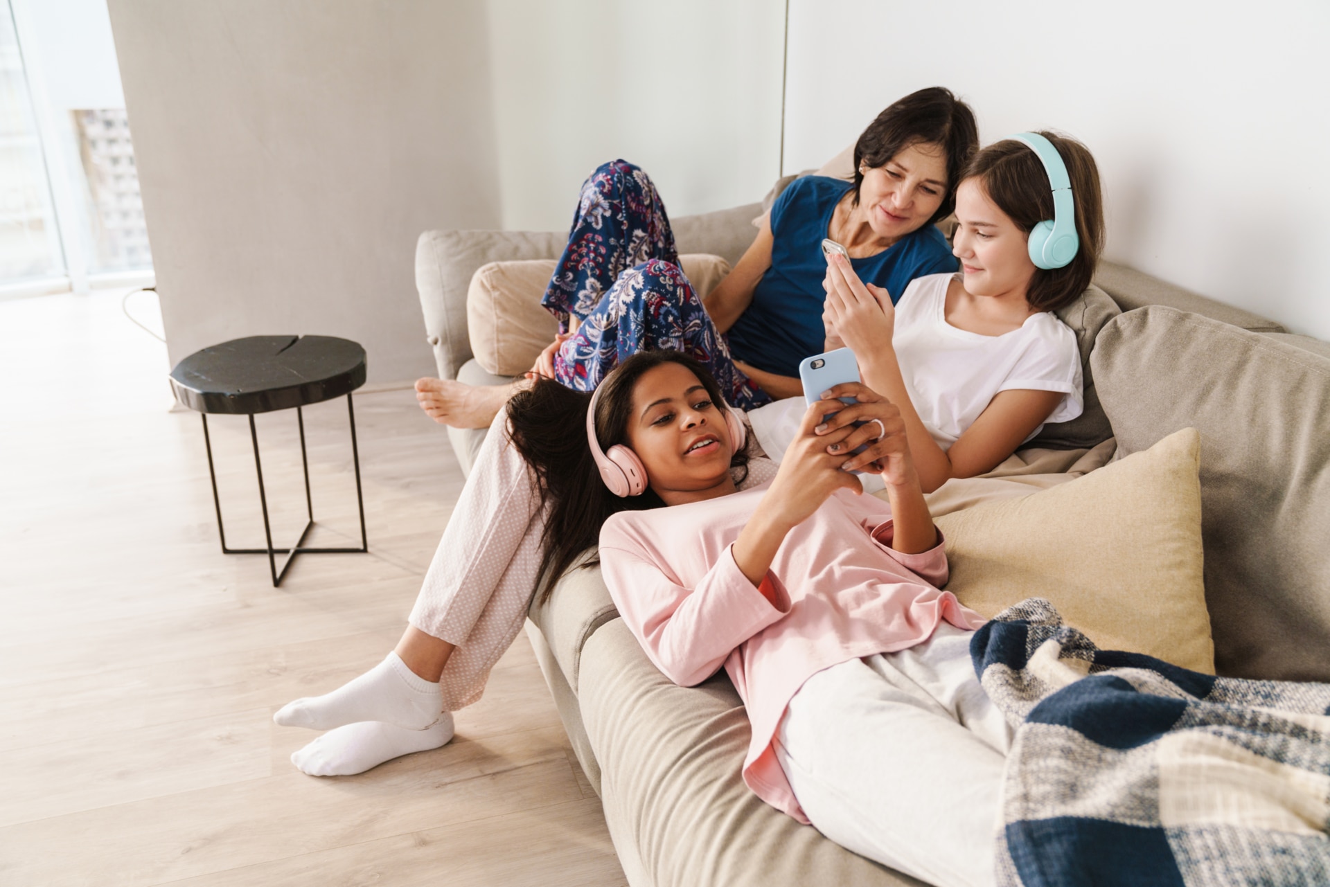 Woman and her daughters using gadgets while resting on couch at home