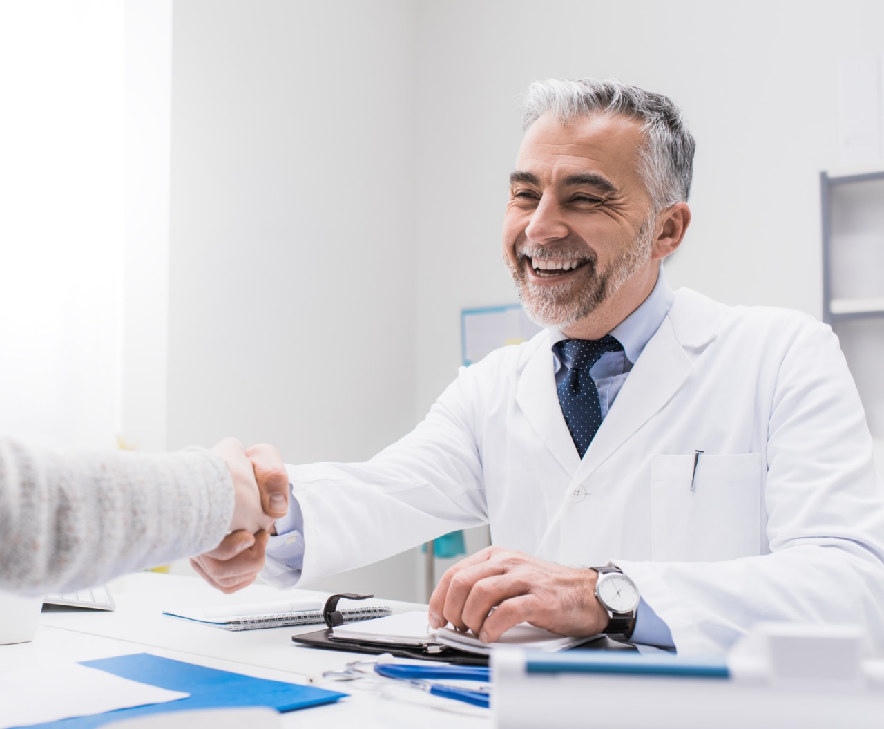 Smiling doctor and female patient shaking hands, healthcare professionals concept