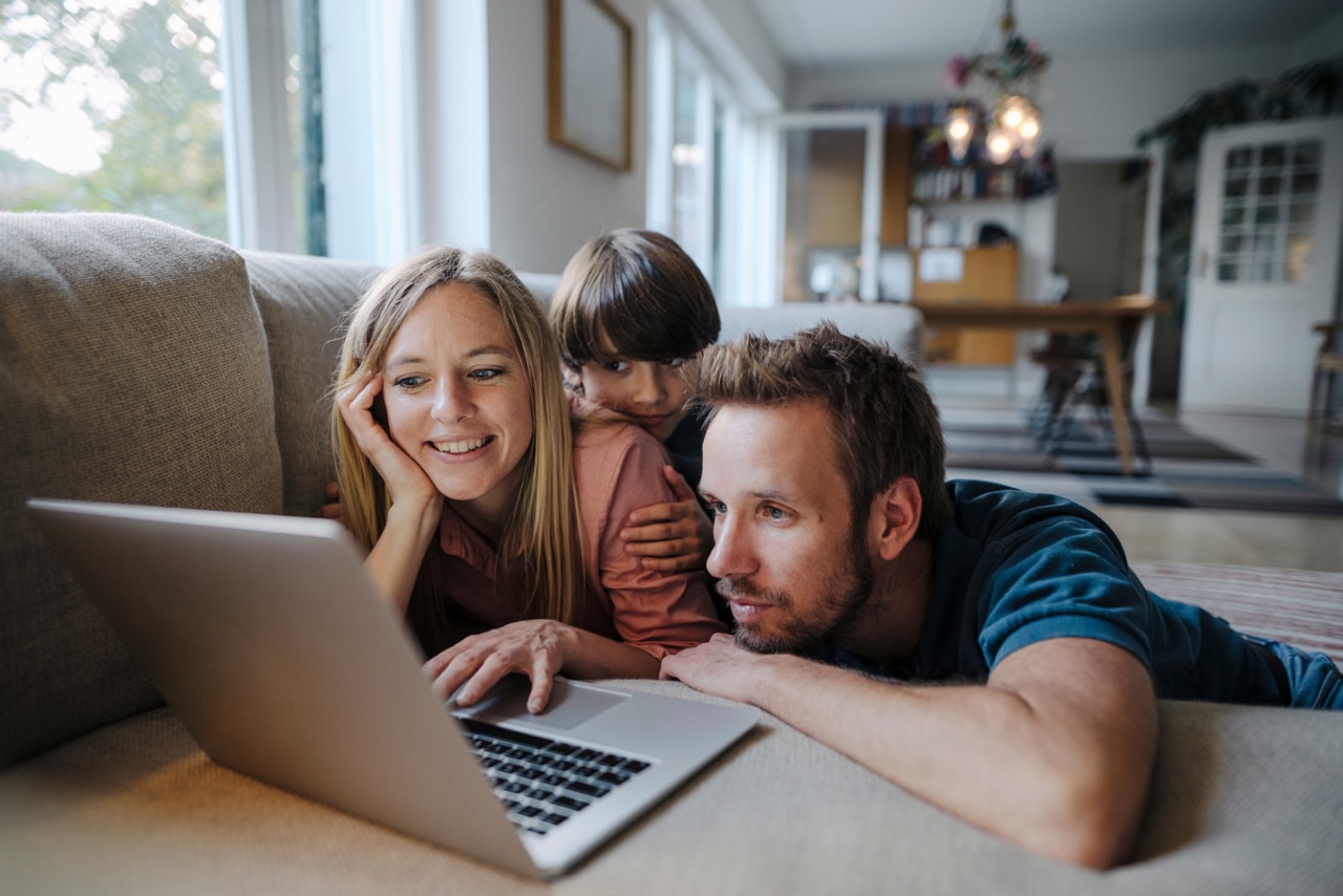 Happy family lying on couch using laptop