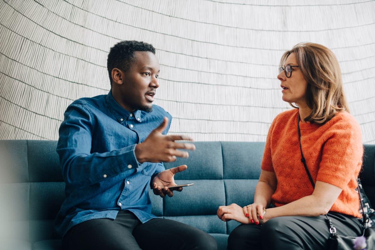 Businessman sharing ideas with female colleague while both sitting on a couch.