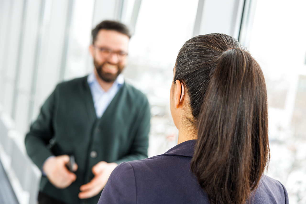 Woman wearing small hearing aid having conversation in hallway Woman wearing small hearing aid having conversation in hallway