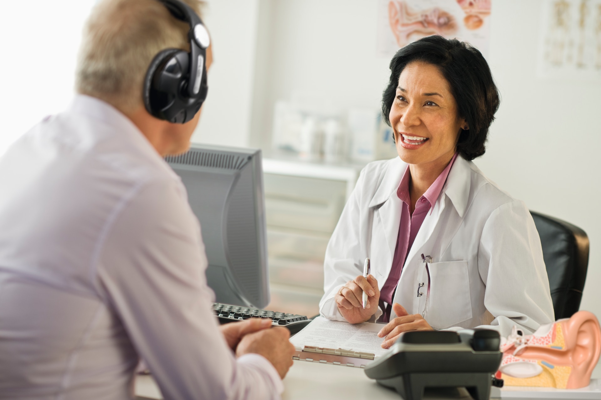 Female audiologist talking with her middle aged male client who is wearing headphones.