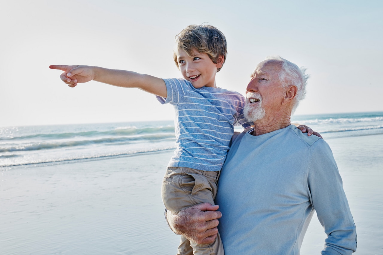 Grandfather carrying grandson on the beach